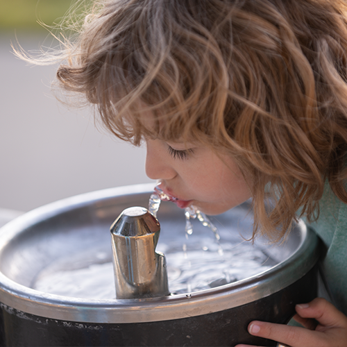 A child drinks from an outdoor water fountain
