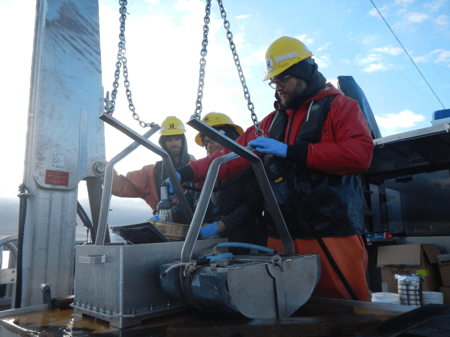 Image of scientists with dual van Veen grab samples. One will be used for physical and chemical parameter analysis and the other is in a large tub to be screened and used for benthic infauna analysis.