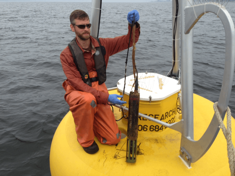 A marine scientist pulling a sensor from a buoy.