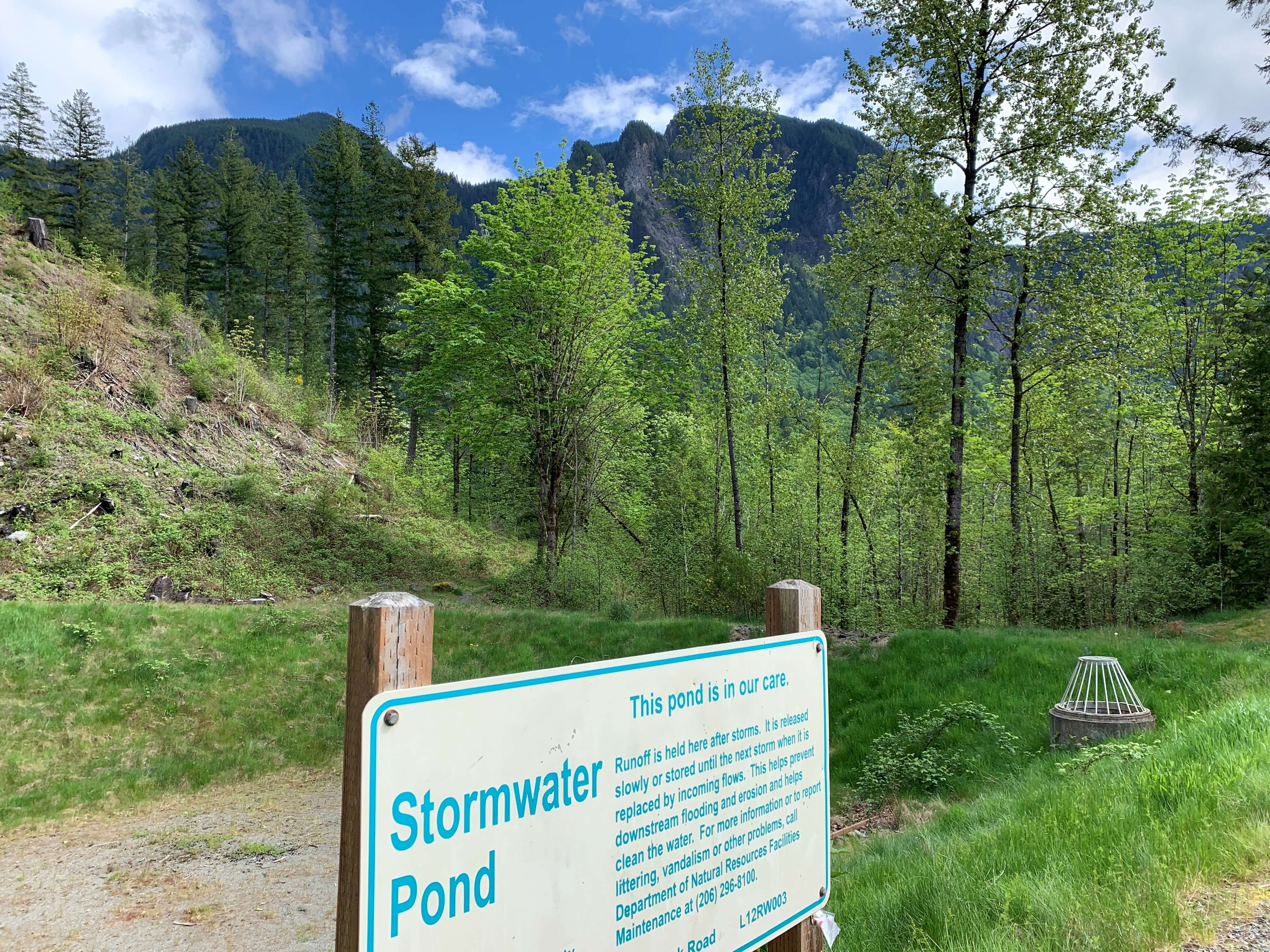 Stormwater facility in North Bend. Stormwater pond signage in front and trees and mountains in the background.