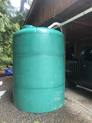 Tall green cistern collecting rainwater from a car port. 