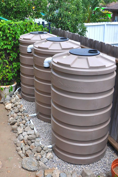 Three brown cisterns, or above-ground water storage tanks, set up along the edge of a fence.