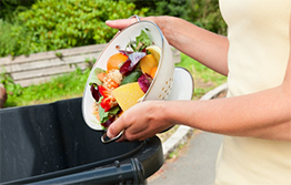Woman disposing food in a solid waste pickup bin for materials that can be composted 