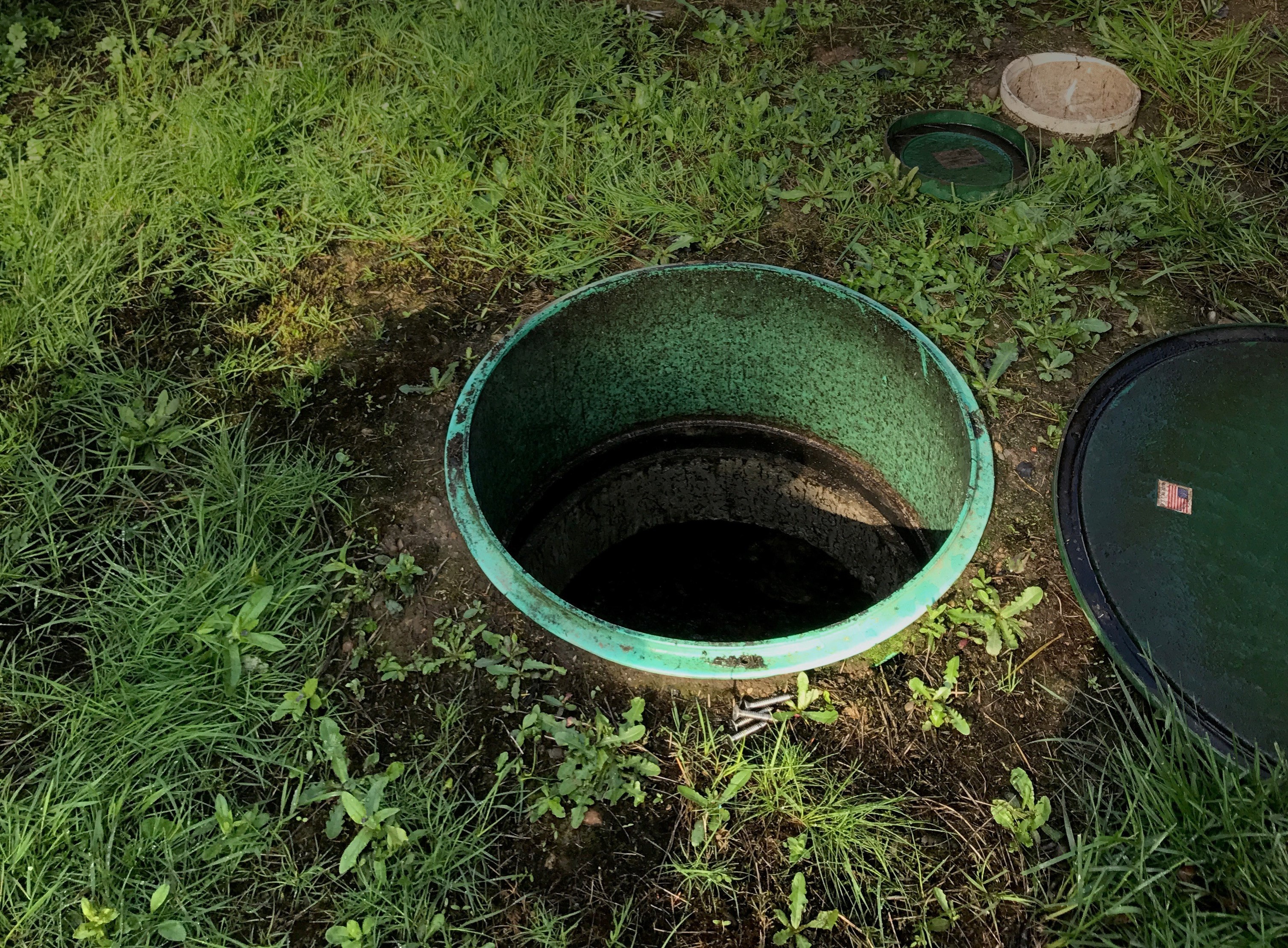 Open green pipe coming up from the ground with grass around it.