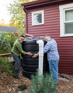 Two happy rainwater harvesters hugging a cistern. The cistern collects rainwater from their roof.