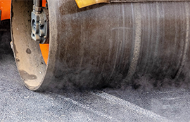 A steamroller flats fresh asphalt on a new regional trail