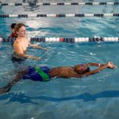 A man coaches a child in a swimming pool on how to float on their back.