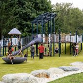 A group of children play on a castle themed playground with parents standing and watching.