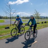 A man and a woman on bicycles ride side by side smiling on an asphalt bike path.