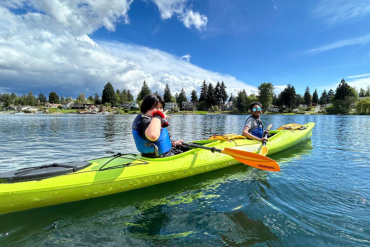 Two children in a bright green sea kayak floating on the water smiling at the camera on a sunny day. 