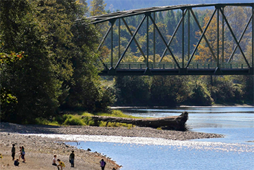 People stand on a riverbank beneath a bridge