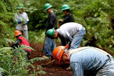 A group of hardhat-wearing staff break ground on a trail