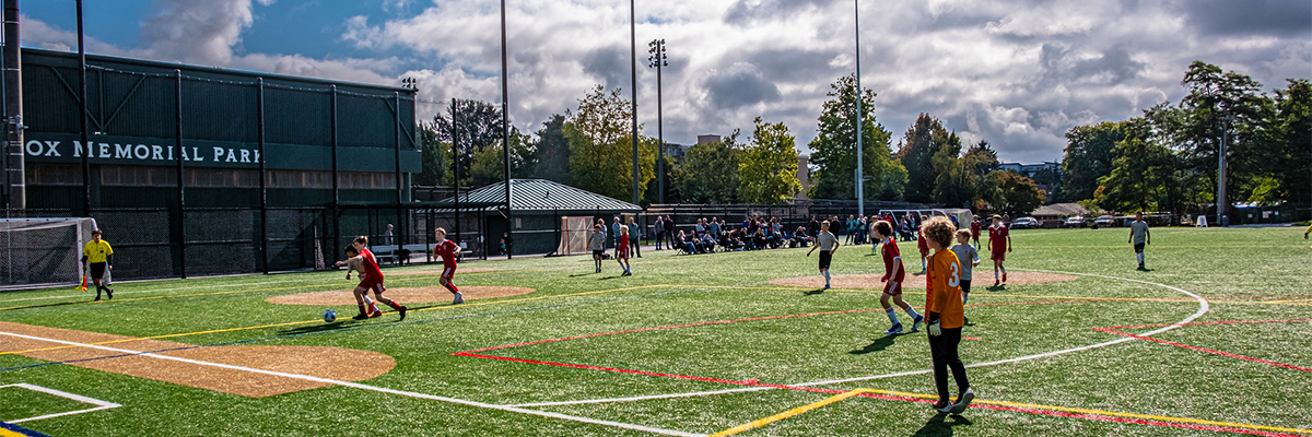 Kids play on a turf soccer field next to Mel Olson Stadium