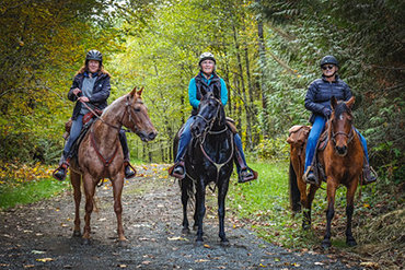 Three people on horseback face the viewer on a Taylor Mountain trail