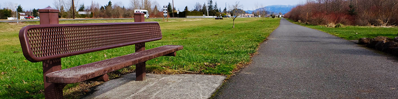 A metal bench is alongside the Foothills Trail with bare trees in the distance