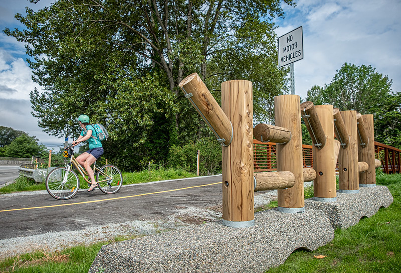 A cyclist rides past a wooden sculpture on the Lake to Sound Trail