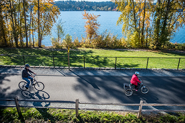 Two people ride their bikes along the East Lake Sammamish Trail with the lake in the backgoround