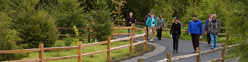 A group of people stroll along the paved trail with rough-cut wooden railings on either side