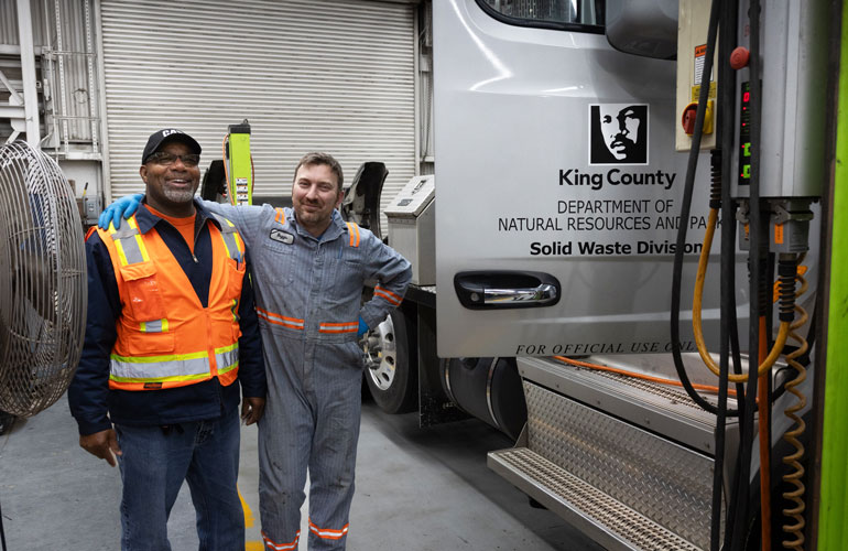 A truck driver and a mechanic pose in front of a King County Solid Waste Division semi truck