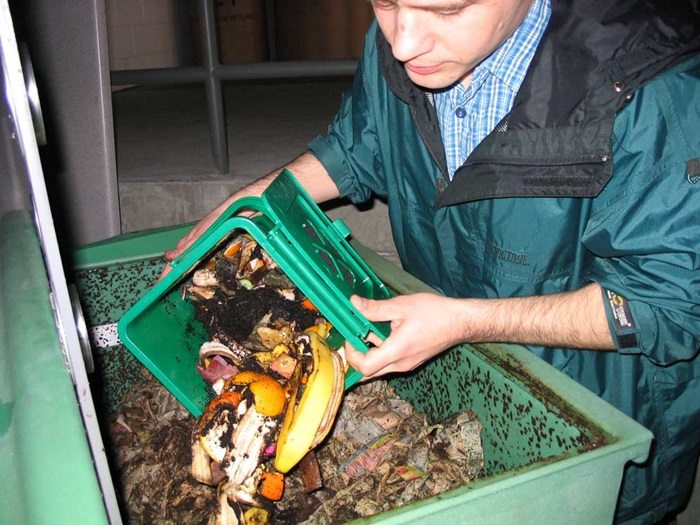 A man transfers food waste, including bananas, from a small compost container into a large compost container.