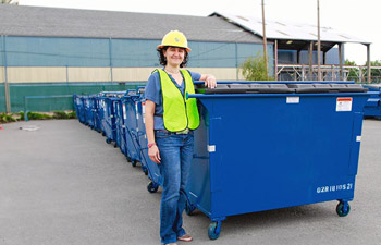 Solid waste worker standing in front of a 2-yard garbage dumpster