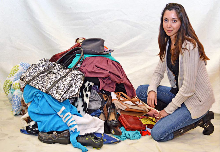A woman kneels next to a variety of clothing items and textiles