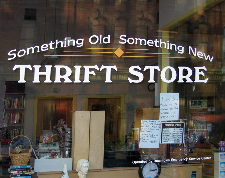 The front window of a thrift store is pictured in front of textiles and some home items.