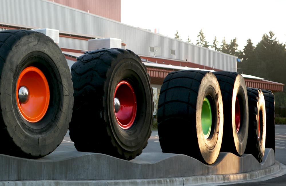 An art installation displays six industrial sized tires, each with the wheel painted a different color, set along a gentle curve