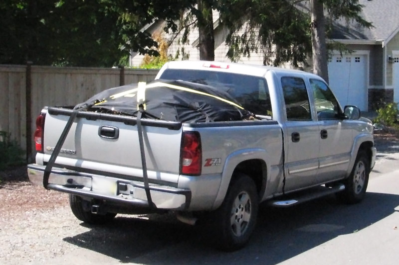 photo of a properly secured load - a load of yard waste covered with a black tarp and securely strapped down in the bed of a silver pickup