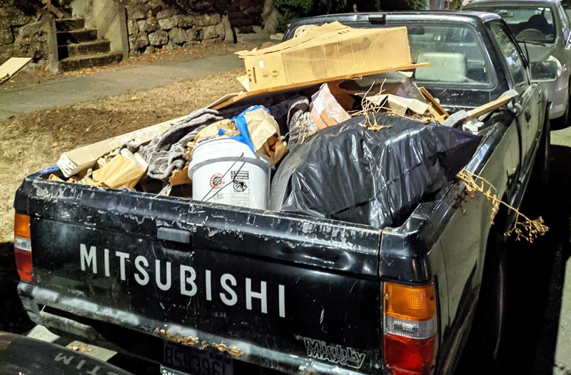 photo of an unsecured load - miscellaneous garbage loose in the bed of a black pickup truck