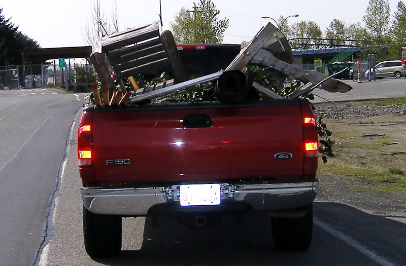 photo of an unsecured load - contractor tools and an extension ladder, loose in the bed of a red pickup truck