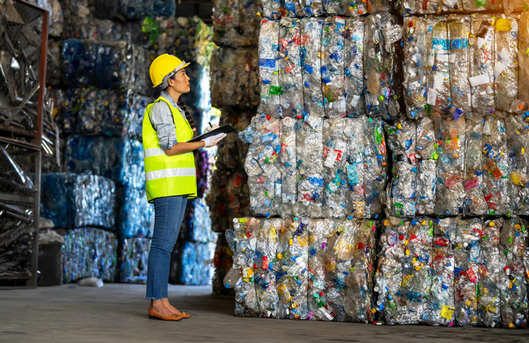 Image showing a worker with a clipboard standing in front of multiple pallets of crushed, baled plastic bottles.
