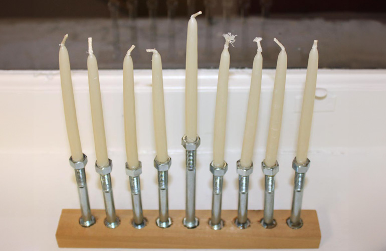 homemade menorah with a wooden base, nut and bolt candle holders, with candles inserted
