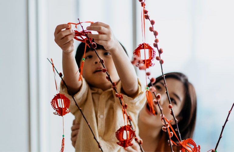 Image of a mother holding a child in the air while she hangs decorations on a branch