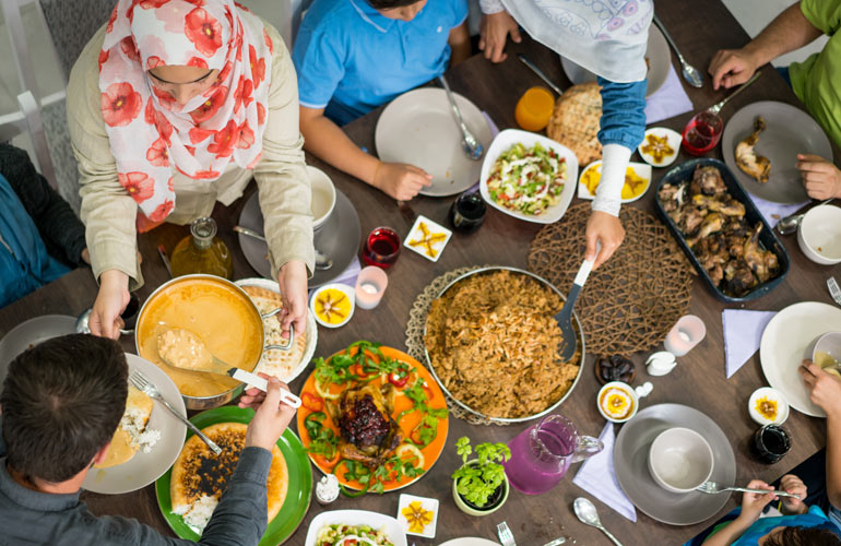 overhead view of several people sitting around a table - sharing multiple dishes for Ramadan