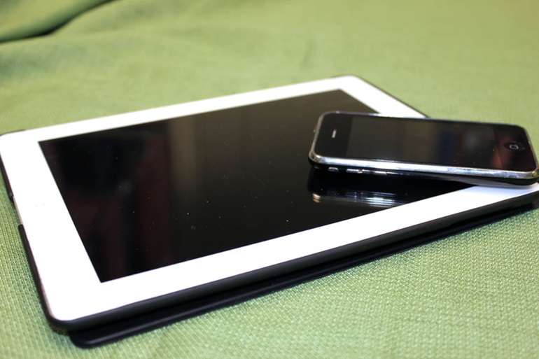 A phone laying diagonally on top of a tablet with white trim laying on top of a green blanket