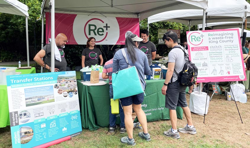 Image of King County Solid Waste Division employees in a booth, promoting the Re+ (zero waste) program at a community event