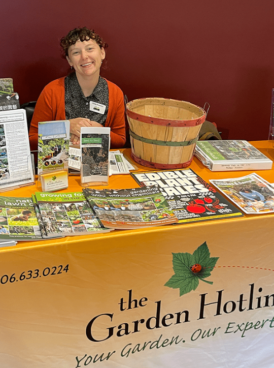 A person sitting at a table with a yellow Garden Hotline banner and chemical-free gardening materials