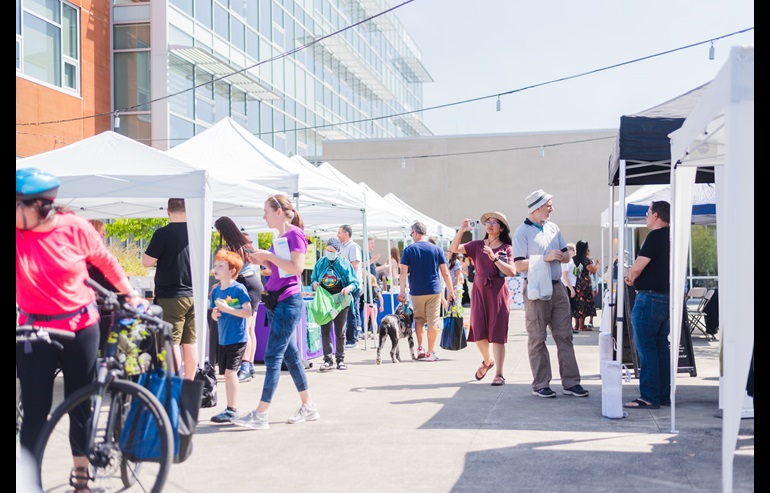 A photo of community members at a street festival with white tents in an open lot