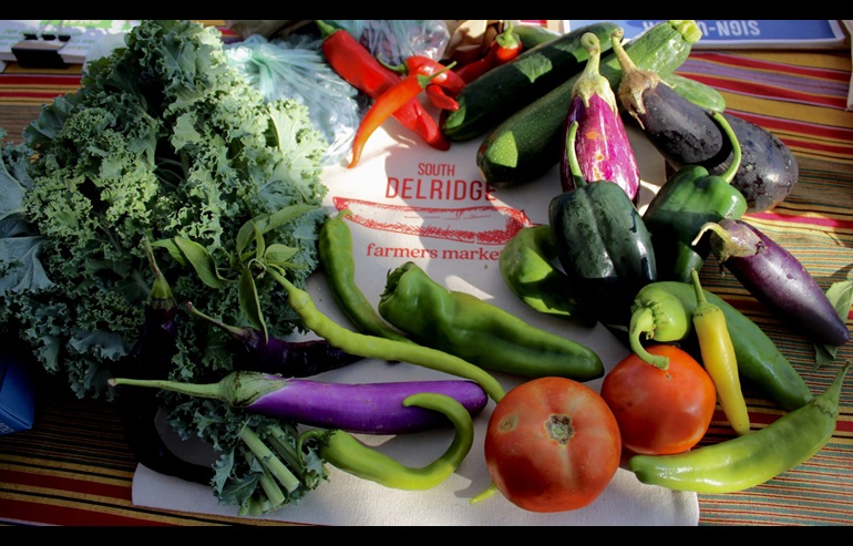 A sign that reads "South Delridge Farmers Market" is surrounded by vegetables on a table