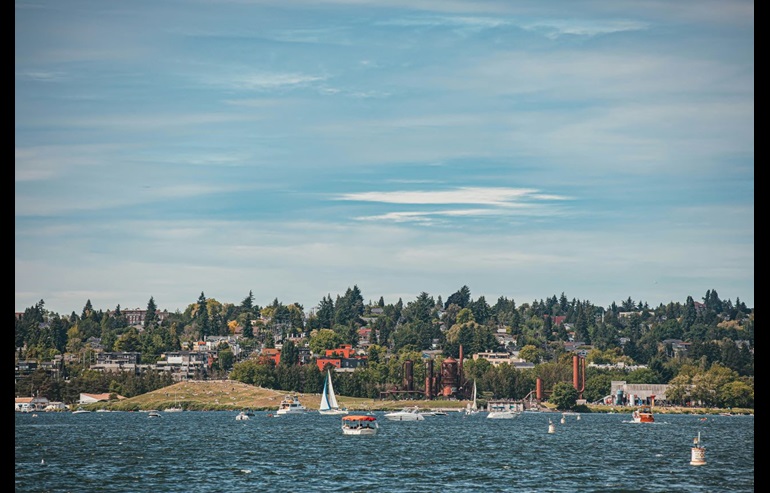 A view from Lake Union in Seattle, Washington looks out at Gas Works Park. Sailboats and buoys are in the foreground.
