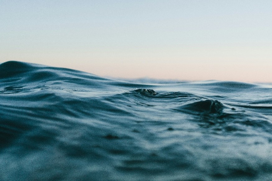A horizontal view of water with blue-pink sky above