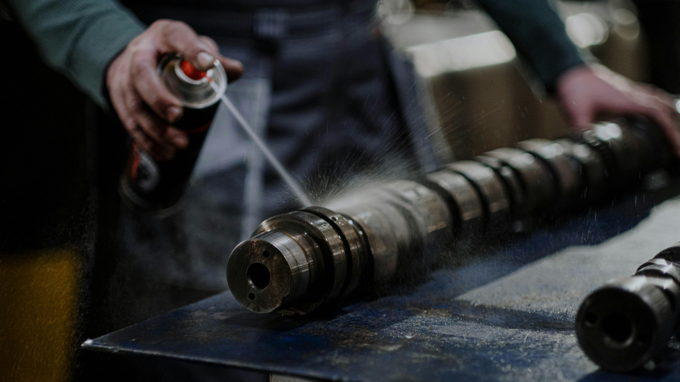 A person sprays a solution from an aerosol can onto a dirty machine part to clean it