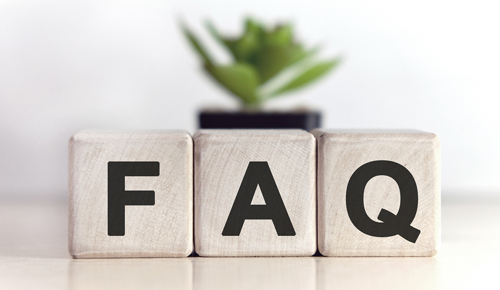 Three wooden blocks spell out "FAQ" in front of an out of focus plant