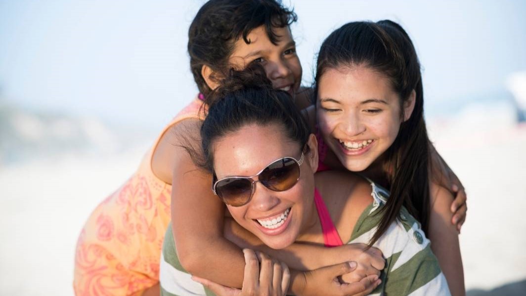 A mother and her two young daughters are laughing and hugging.