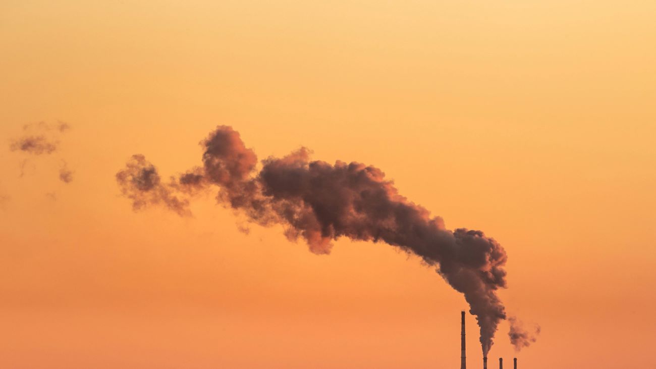 An image of a smokestack billowing a cloud of smoke across an orange sky