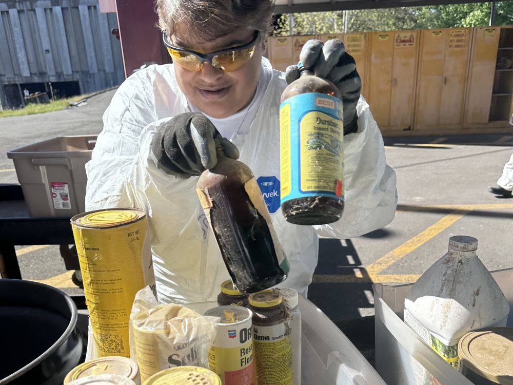 A Haz Waste Program employee in protective gear sorts hazardous products into plastic bins.