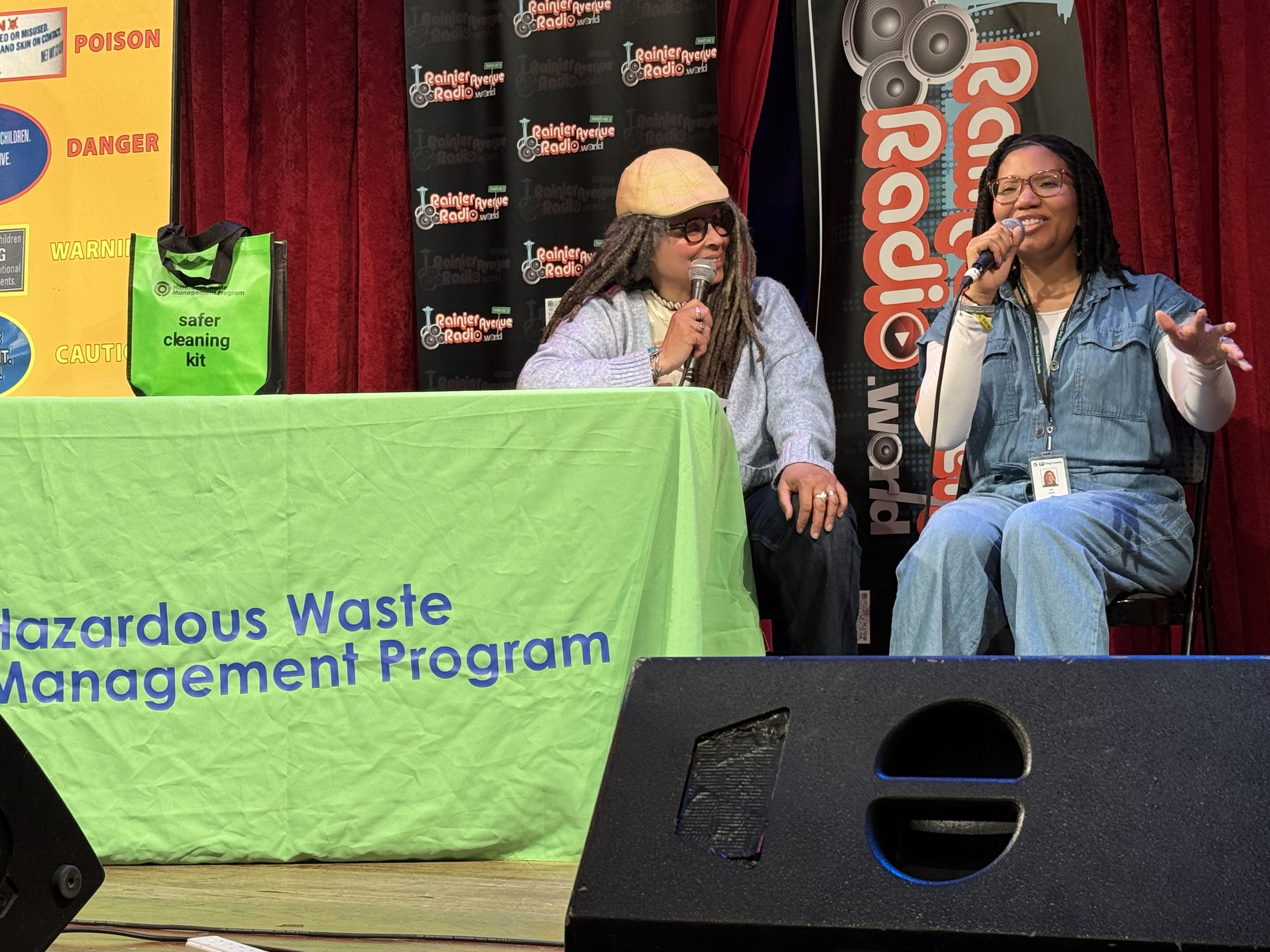 Two women speaking into microphones on stage at a Rainier Avenue Radio event.