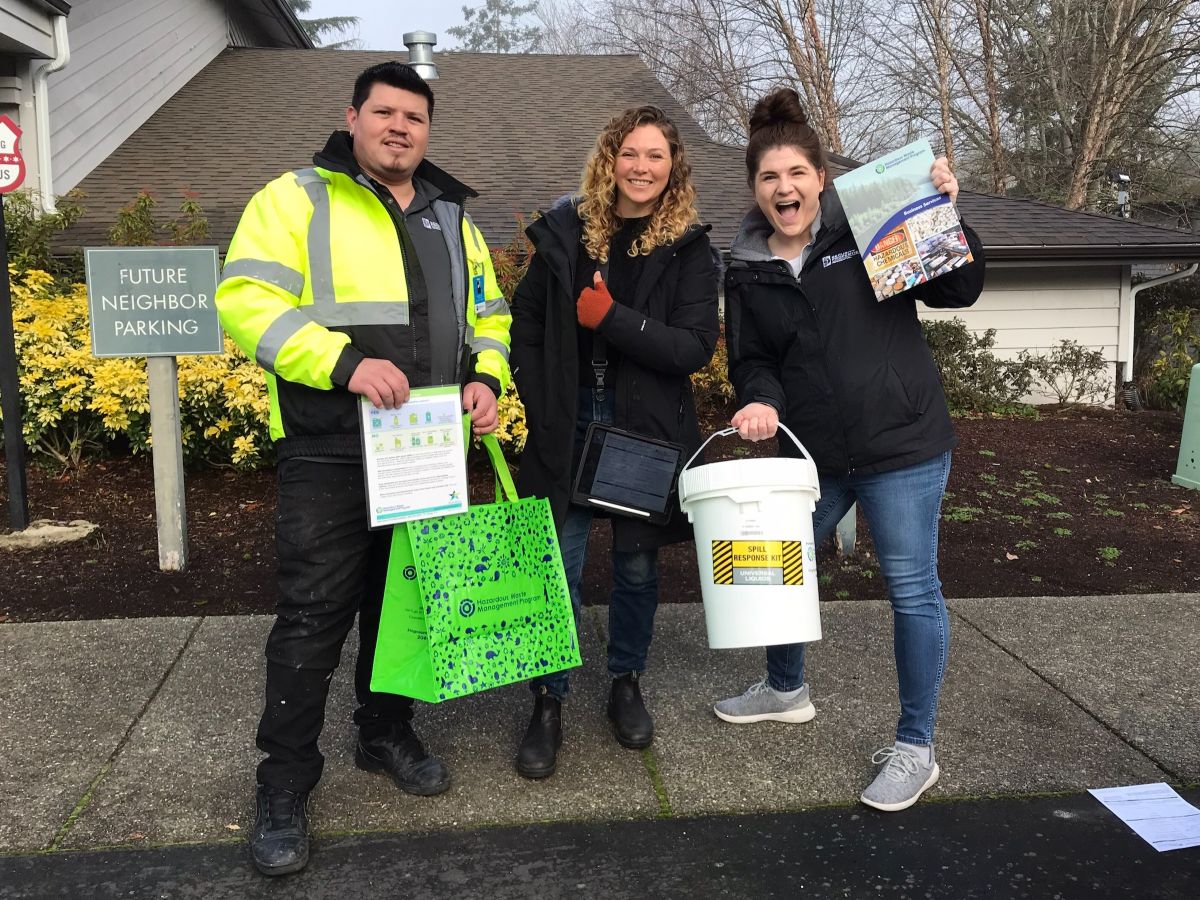 A Haz Waste Program employee poses with two staff members of a local housing agency. The staff members are holding hazardous waste management kits for small businesses.