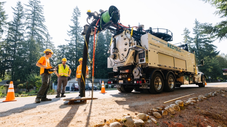 Three King County staff personnel with personal protection equipment (bright vests, hard hats, work boots) standing next to an open sewer maintenance hole and new sewer cleaning truck.